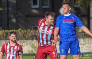 Two football players jumping in the air to head a ball whilst a third player looks on